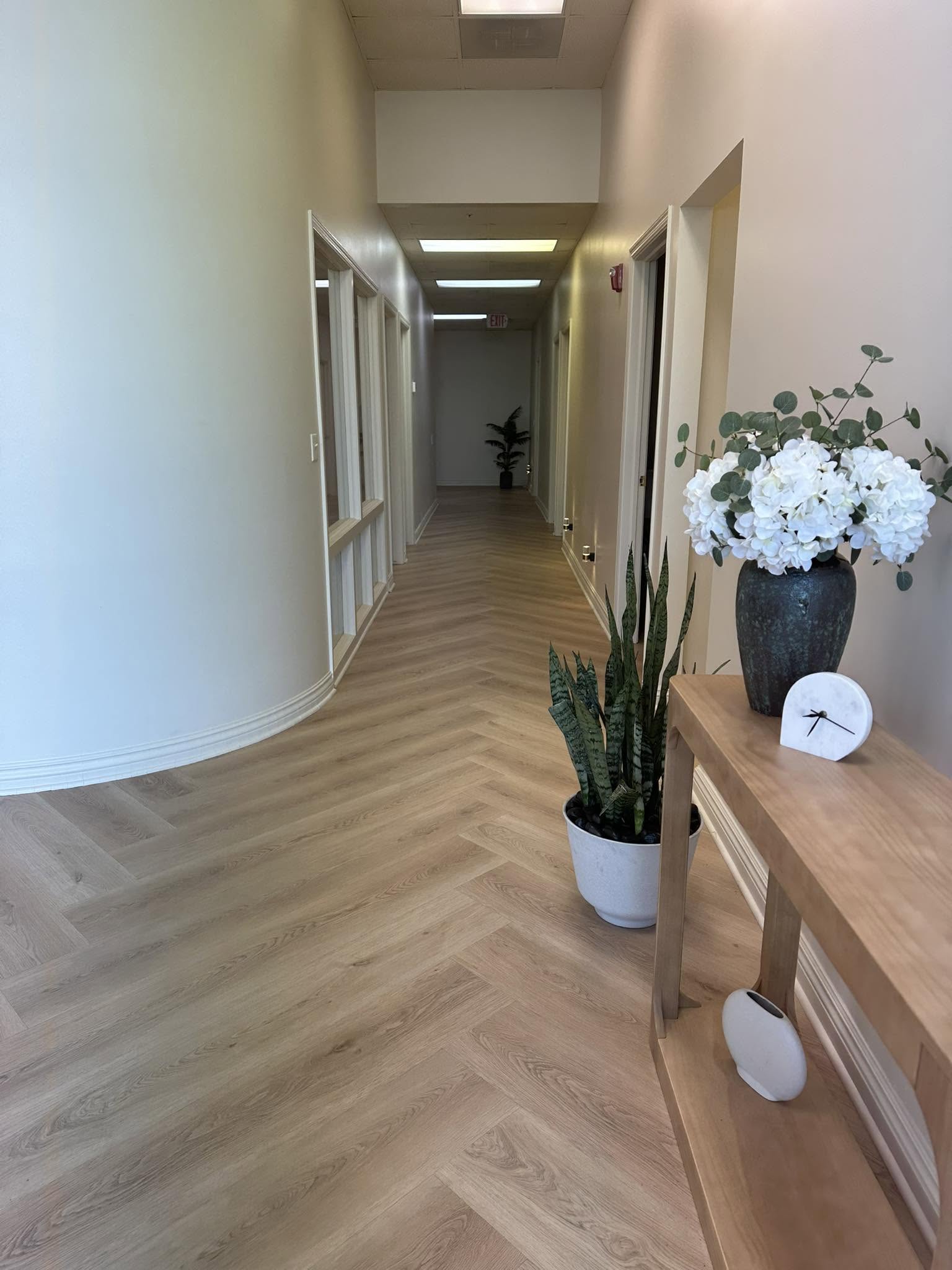 Calm hallway leading to treatment rooms at Omaha Massage & Wellness Center, with wood flooring and fresh flowers